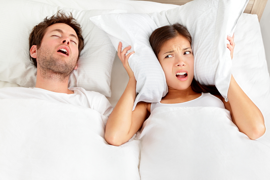 man snoring loudly, woman holding pillow over ears to block noise. Greenville, NC snoring treatment